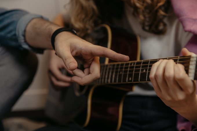 Photographie en plan rapproché d'une jeune femme apprenant des accords de guitare avec son instructeur