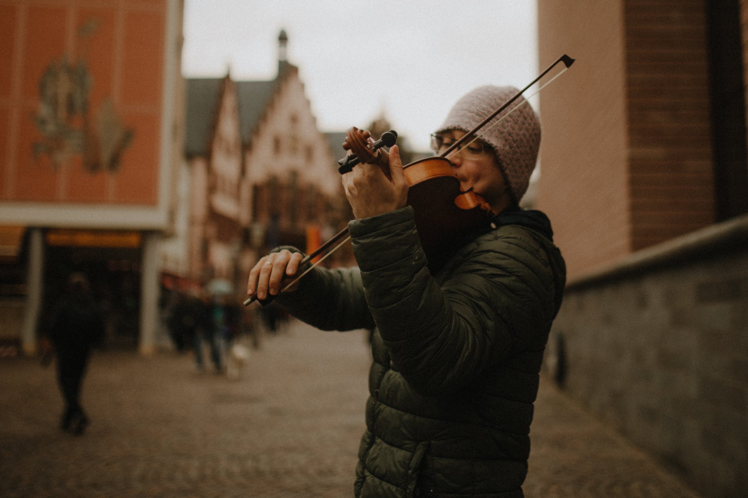 Un jeune homme d'origine asiatique avec un bonnet et une doudoune jouant du violon dans une rue piétonne
